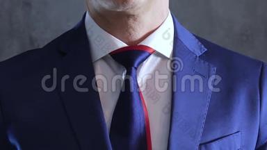 穿蓝色西装的人的手臂在灰色混凝土墙的背景上将领带系在脖子上